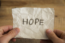 hands holding a crumpled paper with the word hope.