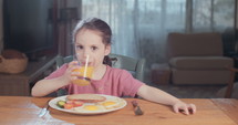 Little girl drinking juice sitting at home.