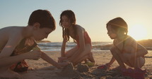 Three kids playing on the beach building sand castles together