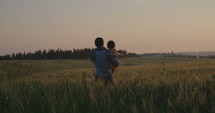 mother and young daughter walking and playing in a field during sunset