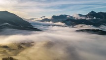 Aerial time lapse view of clouds rolling over mountains at sunrise.