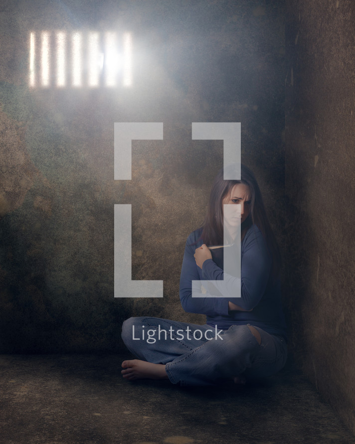 a woman sitting alone in a cell grasping a Bible 