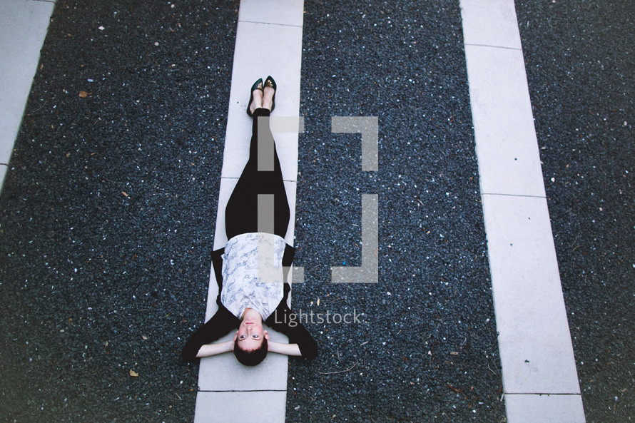 A woman lying on a white line in a parking lot.