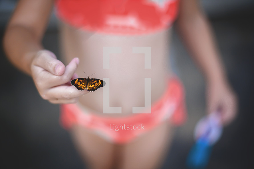 child in a bathing suit with a butterfly on her finger 