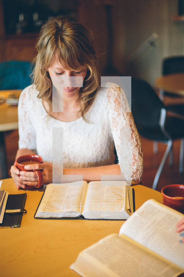 Woman sitting at a table, reading her bible, drinking coffee