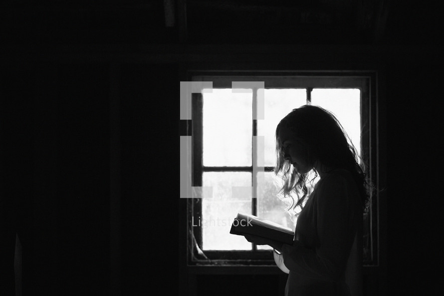 a woman reading in front of a window in a dark room 