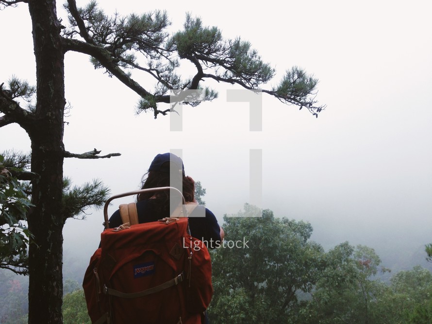 Hiker with a backpack by a pine tree in the mountains at dawn.