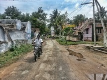 man on a dirt bike on a dirt road in a village 