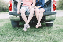 legs of a couple sitting in the back of a pickup truck 