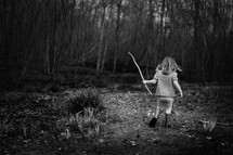 girl walking in a forest holding a stick 