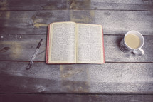 pen, pages of a Bible, and coffee mug 