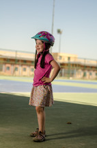 A young girl in a bicycle helmet standing near a school.