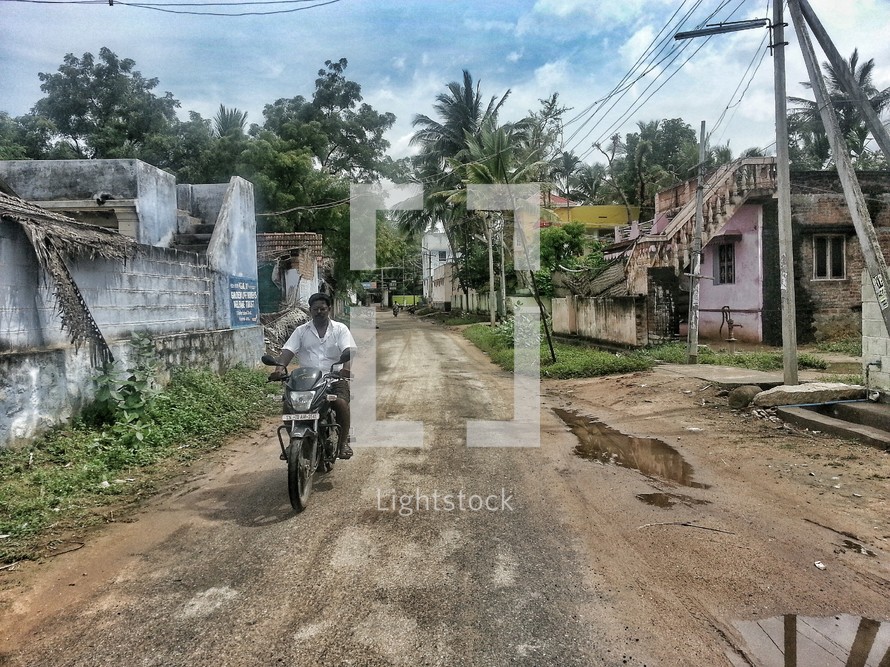 man on a dirt bike on a dirt road in a village 