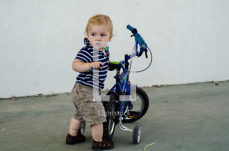 A toddler holding on to a bicycle with training wheels.