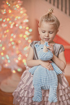a little girl holding a stuffed animal in front of a Christmas tree