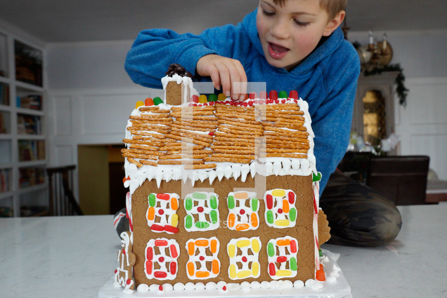 a boy decorating a gingerbread house 