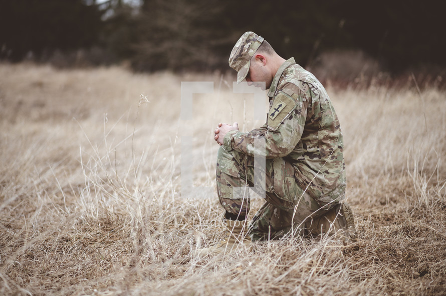 Christian soldier kneeling in a field praying 