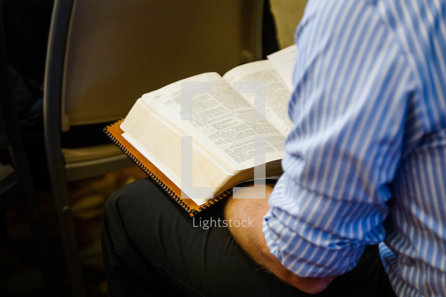 man reading a Bible in his lap at church 