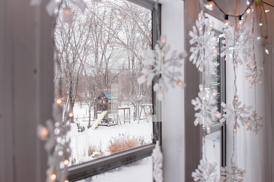 snowflake Christmas lights and snowy scene out a window 