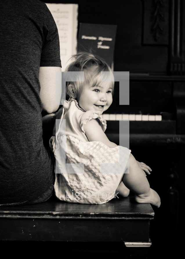 Baby girl listens and smiles while dad plays worship music on the piano.