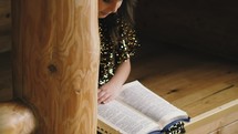a girl reading a Bible in a cabin at Christmas 