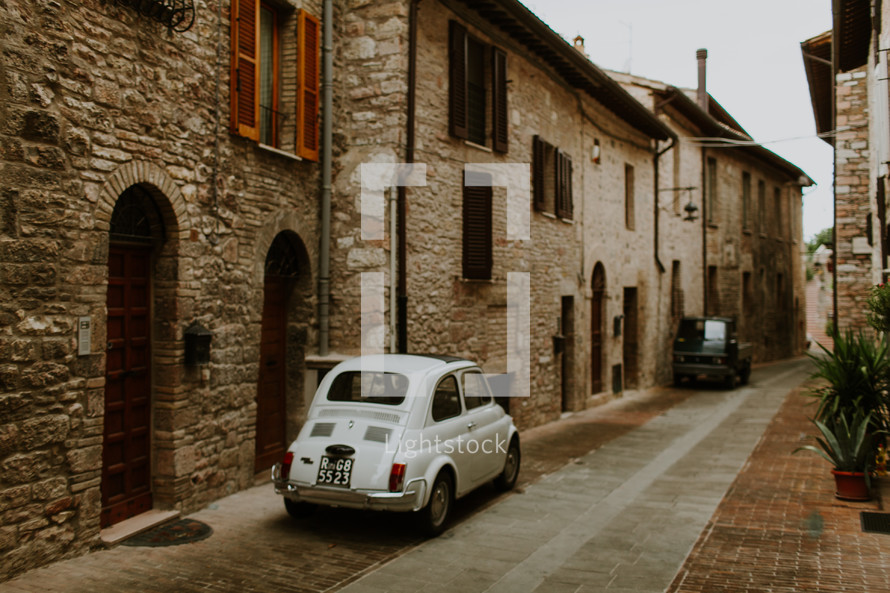 Two small cars parked in a narrow alleyway between old stone buildings.