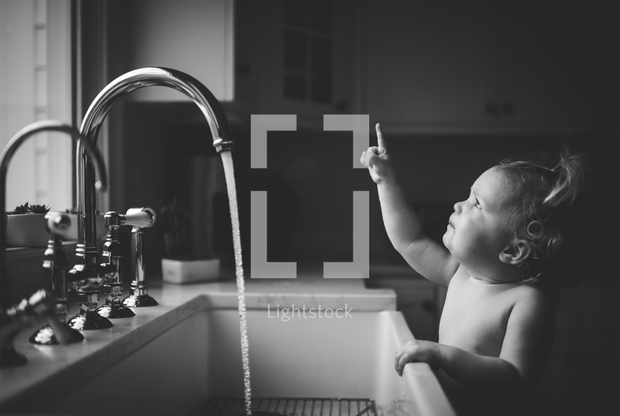 toddler girl playing in water at the kitchen sink