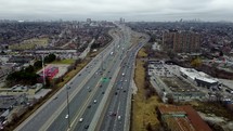 Aerial panning shot of a drone flying over Highway 401 in Toronto on a cloudy day. View of arterial road that across a residentialindustrial area. Slight busy traffic.