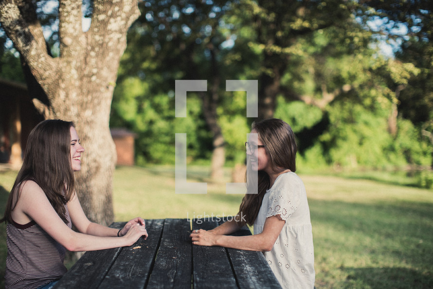 teen girls talking outdoors sitting at a picnic table 