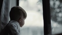 toddler boy looking out a window at falling snow 