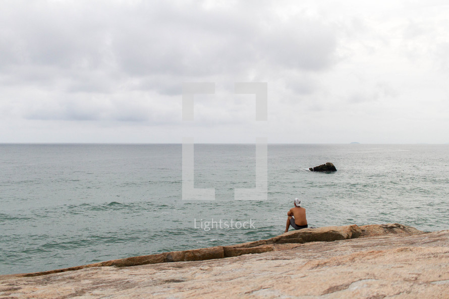 a man sitting at the edge of a shore contemplating 
