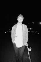 a man standing holding a skateboard at night 