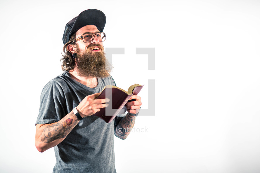 man with tattoos reading a Bible looking up to God 