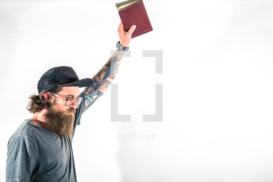 man with tattoos raising a Bible to God 