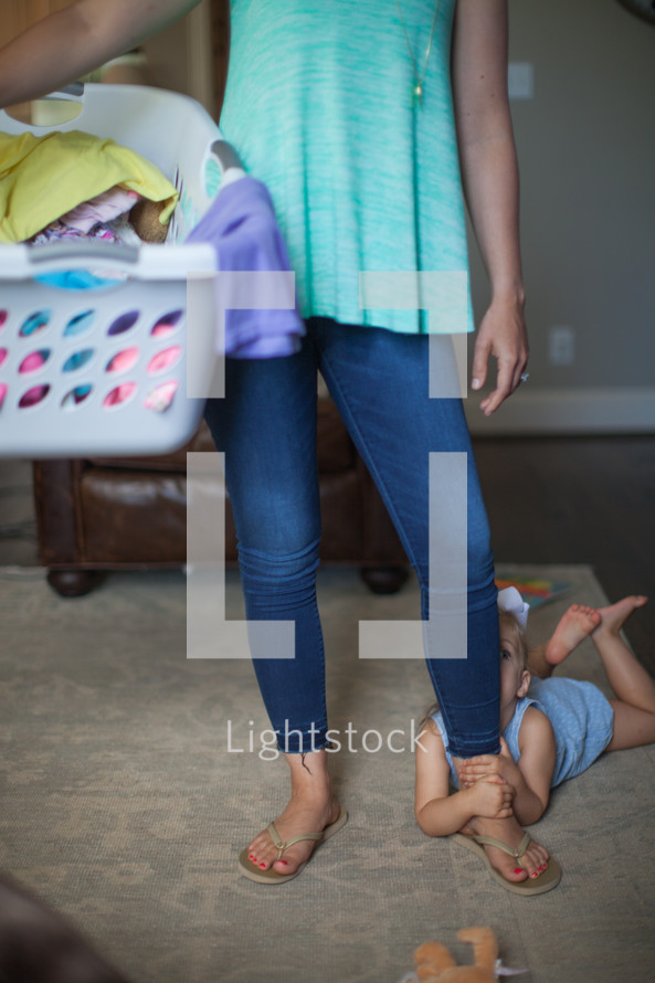 a mother holding a laundry basket and child clinging to her leg 