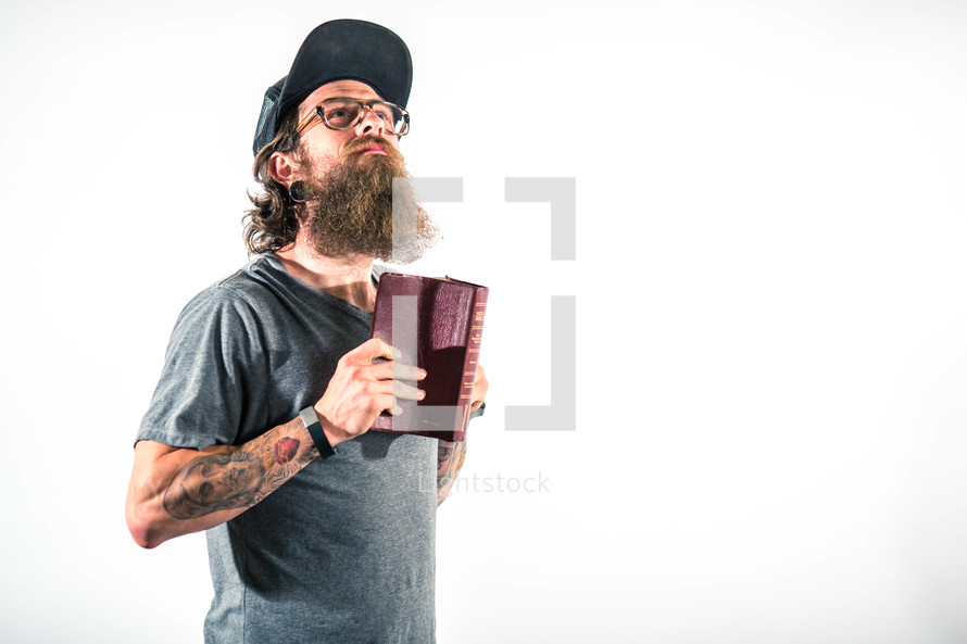 man with tattoos holding a Bible and looking up to God 