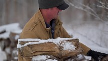 Man picking up firewood from a wood pile in the snow