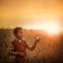 a boy with a toy airplane in a field at sunset 