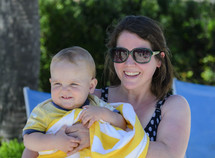 a mother holding an infant wrapped in a beach towel 