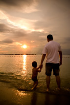 a father and son standing on a beach 