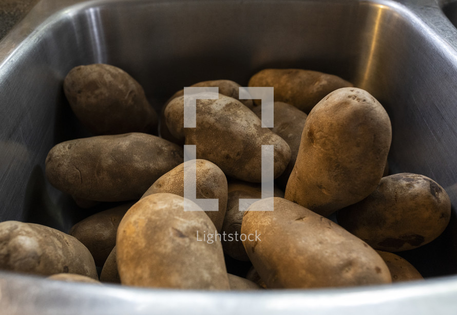A sink full of potatoes waiting to be peeled