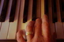 A hand (with wedding ring) plays a chord on a piano