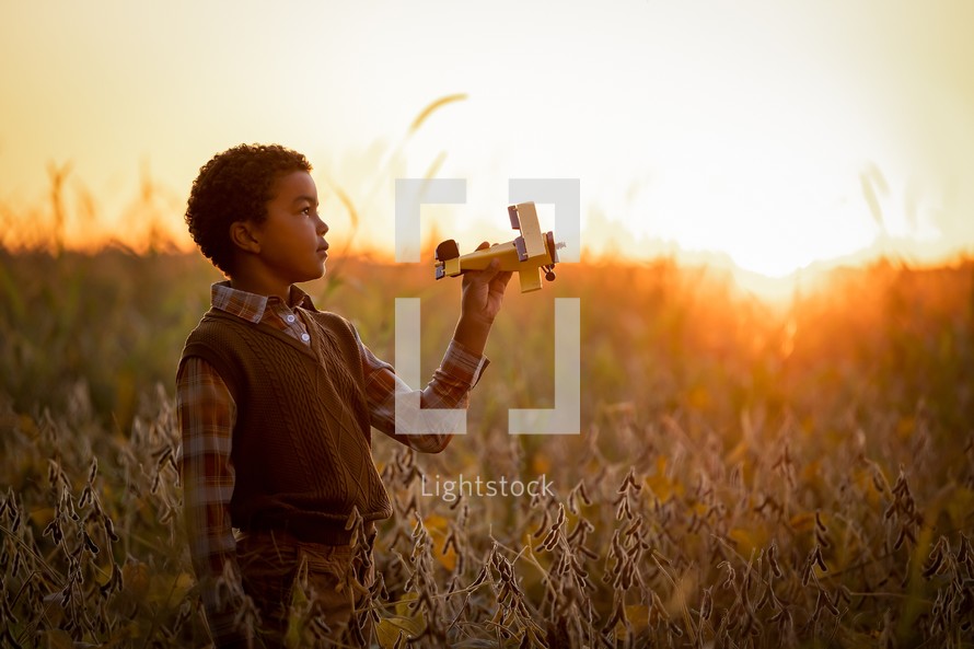 a child with a toy airplane in a field at sunset 