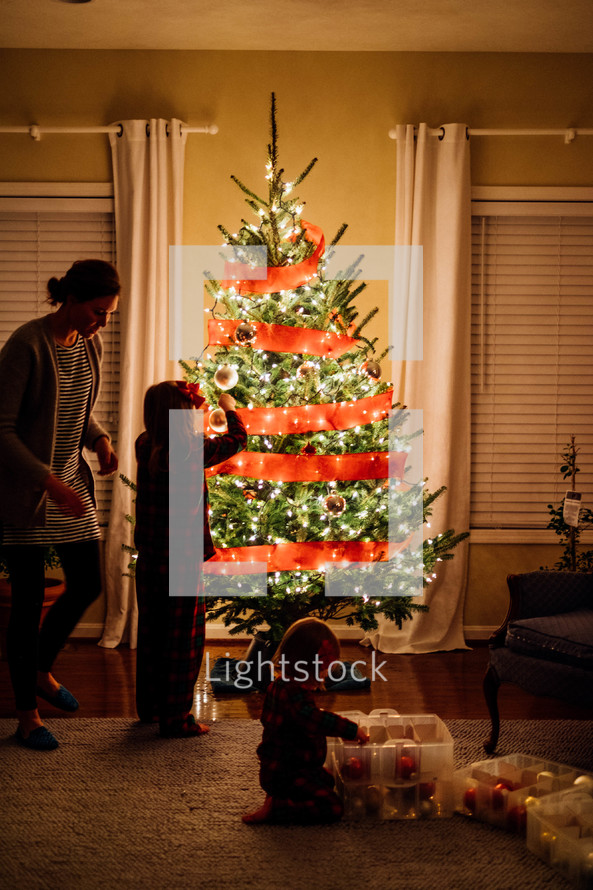 mother and daughters decorating a Christmas tree 