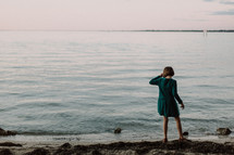 a girl child in a dress standing on a shore 