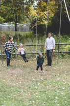 family playing outdoors on a swing set in the backyard in fall