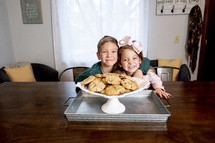 a brother and sister near a plate of cookies 