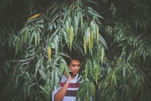 a boy talking on a cellphone hiding from behind leaves 