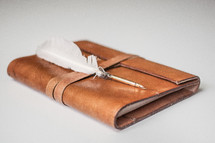 a feather quill pen on a leather journal 
