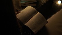 teen girl sitting by a lamp in a dark room reading a Bible 